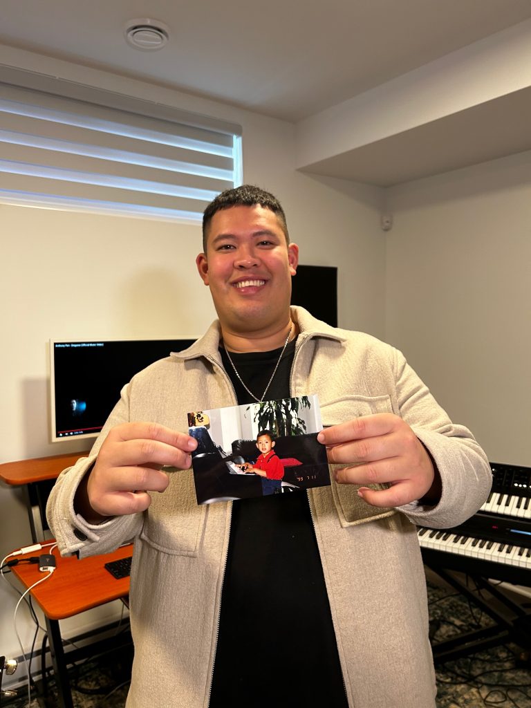 Anthony Pen, holds up a photo of himself playing piano when he was younger, while standing in his studio