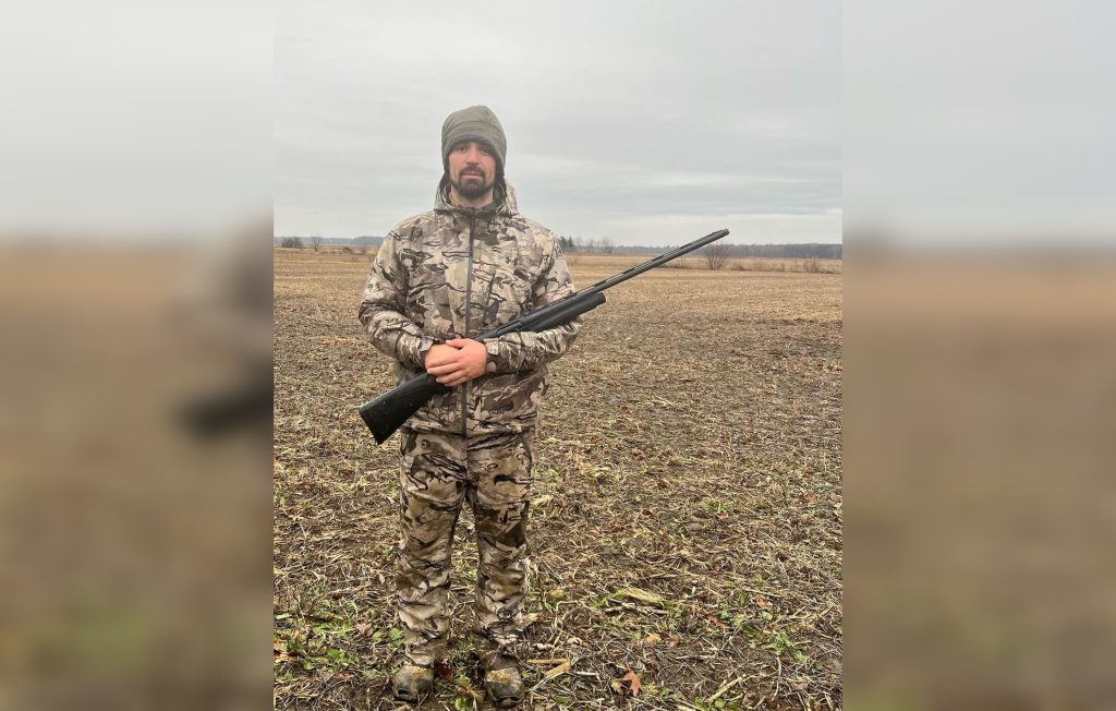 man dressed in camouflage in field holding gun