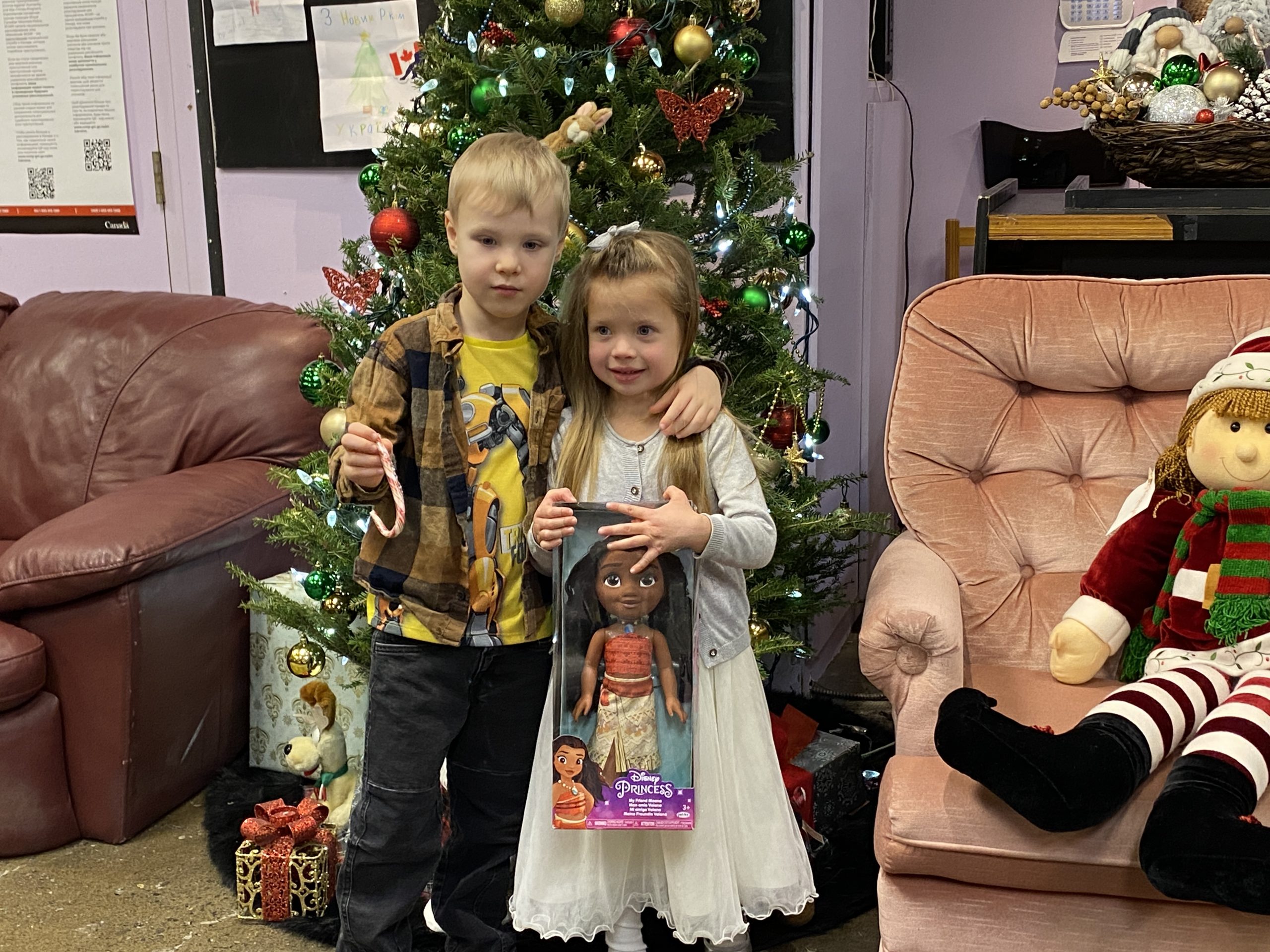 Ukrainian children pose in front of a Christmas tree with presents at the Centre for Ukrainian Newcomers.