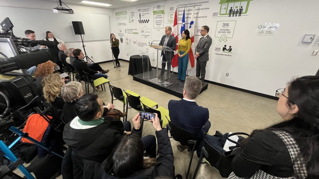 Valerie Plante is seen on a podium with two other men at a press conference