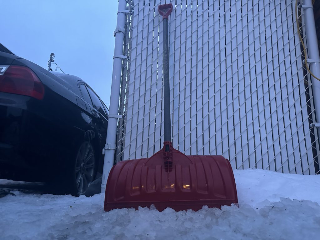 A red shovel is seen leaning against a fence 
