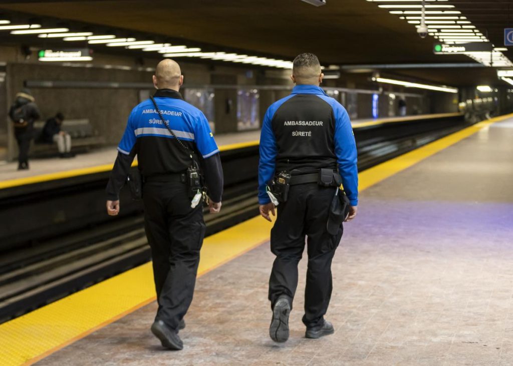 Two Safety Ambassadors are seen with their backs turned walking near the tracks in Place-des-Arts metro