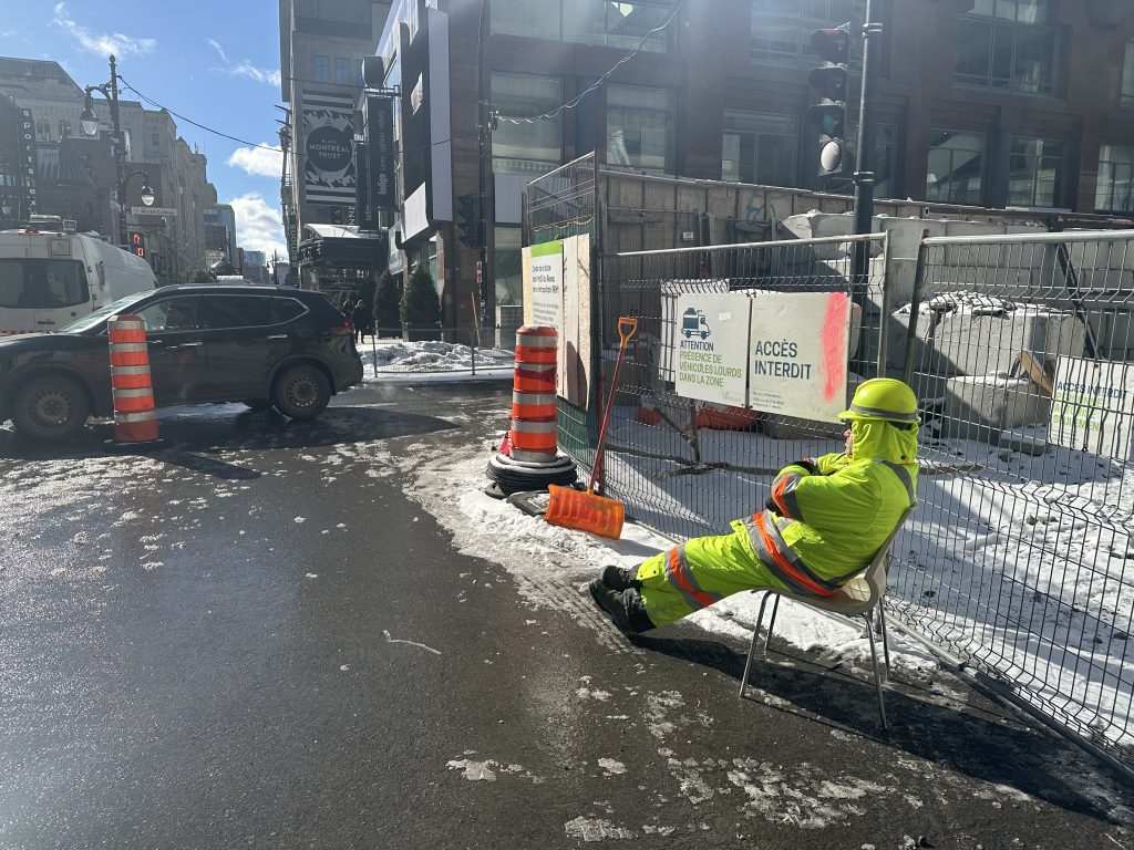 A construction worker  in yellow and orange is seen sitting in a chair on Saint-Catherine Street in Montreal