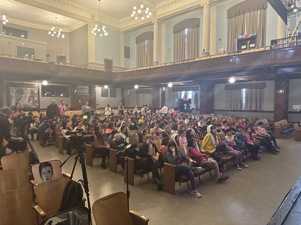 Los estudiantes están sentados para la presentación del Día de la Camisa Rosa en la escuela primaria FACE