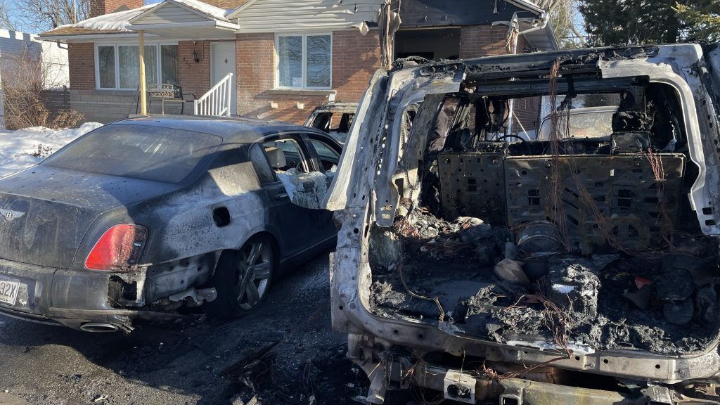 Two cars are seen with fire damage in the driveway