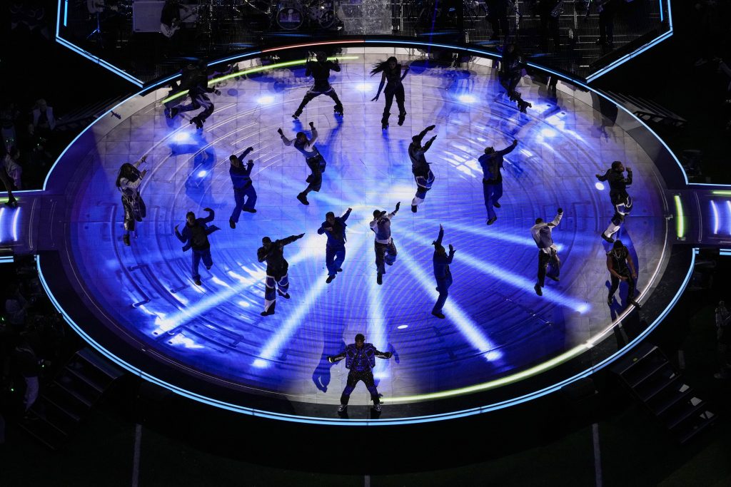 Usher, bottom center, performs during the halftime show on a lit up stage